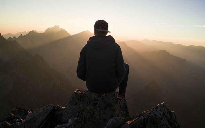 man sitting on rock in mountains looking out